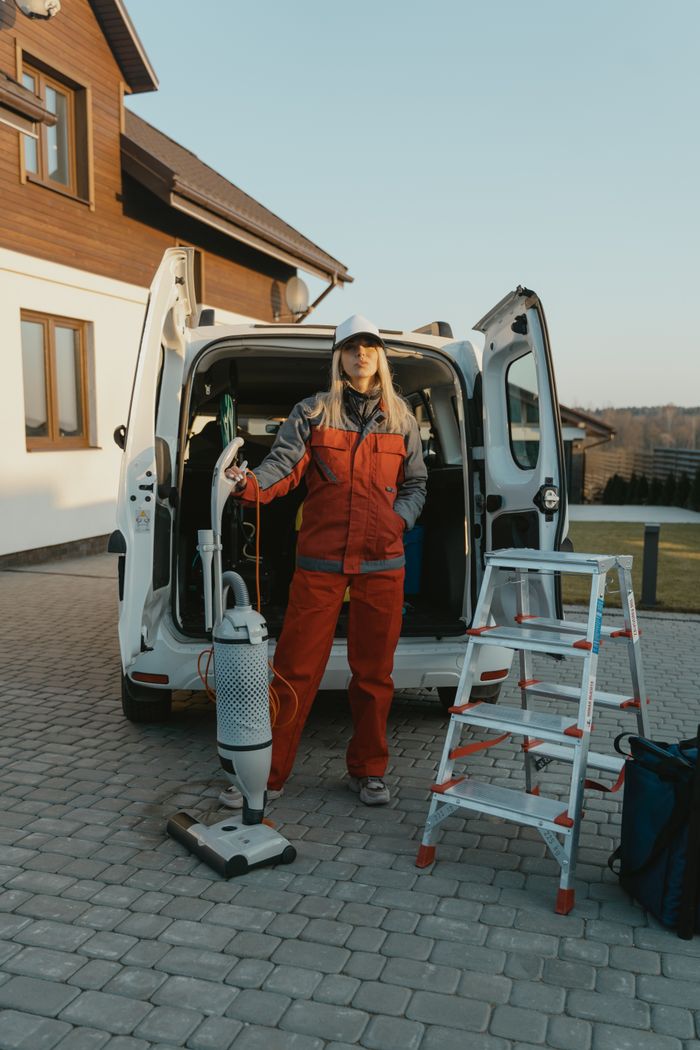 Un agent d’entretien en uniforme se tient près d’un van avec du matériel de nettoyage, devant une maison moderne au coucher du soleil.